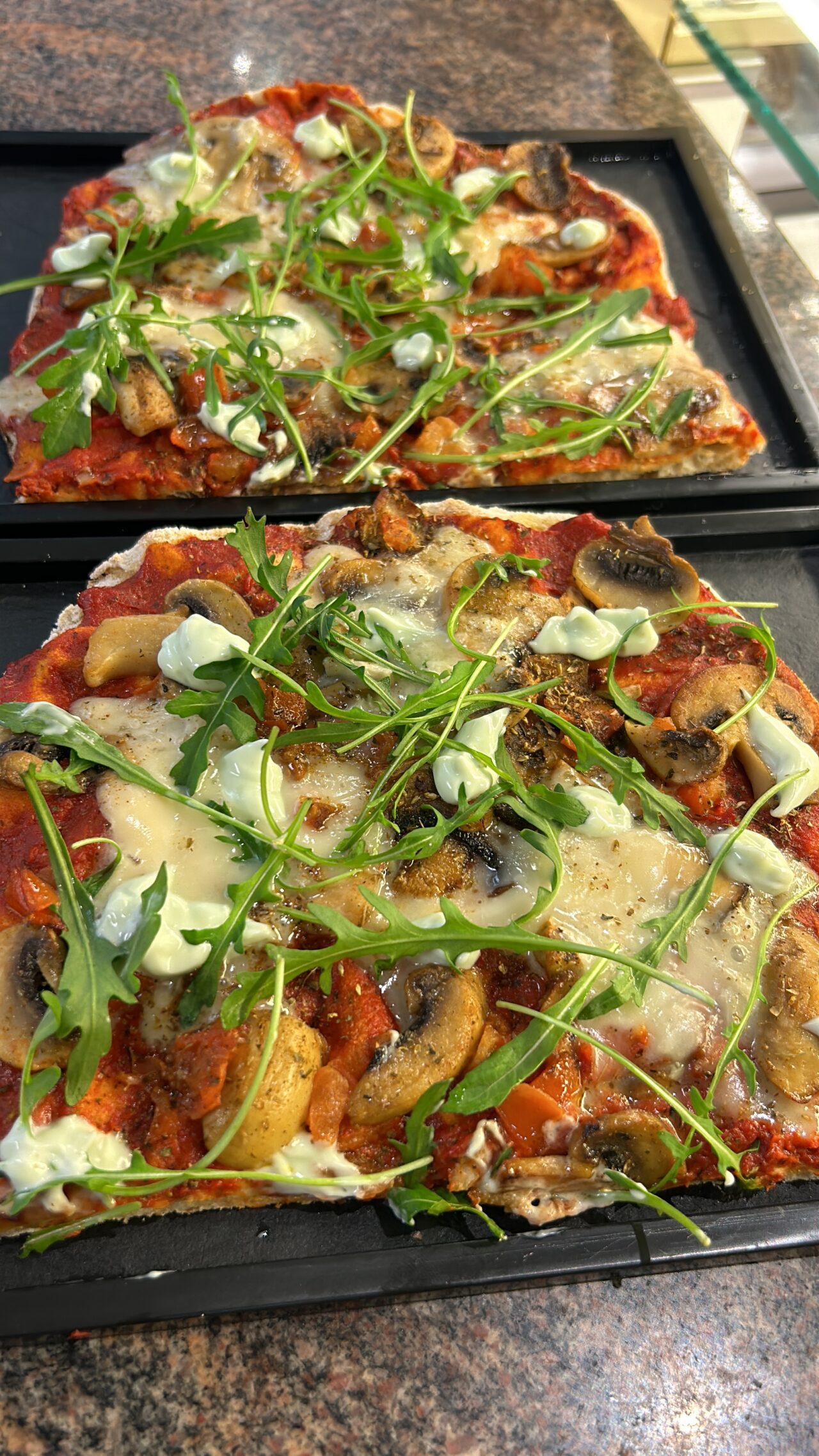 Frische Pizza mit Pilzen, Rucola und Käse auf knusprigem Teig, serviert auf einer schwarzen Backform.