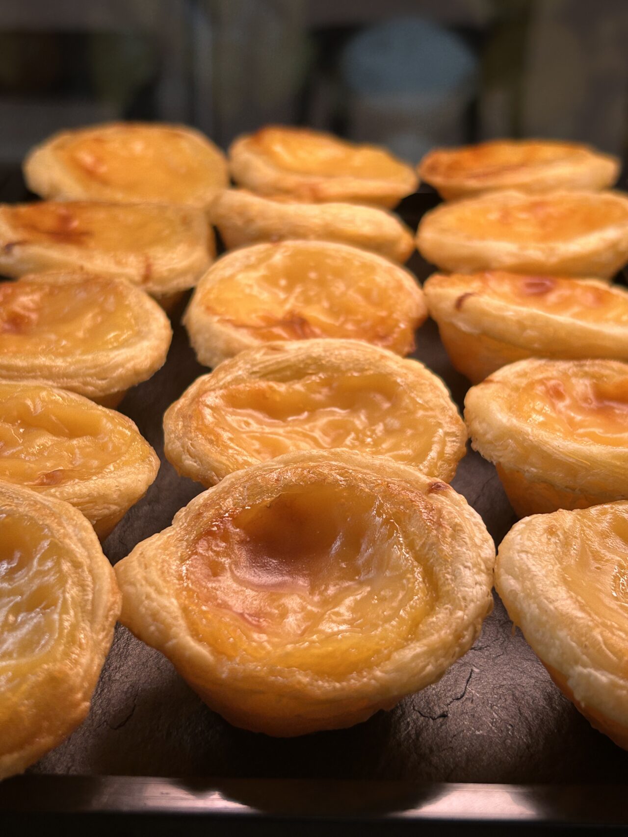 Frische portugiesische Pastel de Nata mit goldener Kruste auf einem Backblech. Perfekte süße Leckerei.