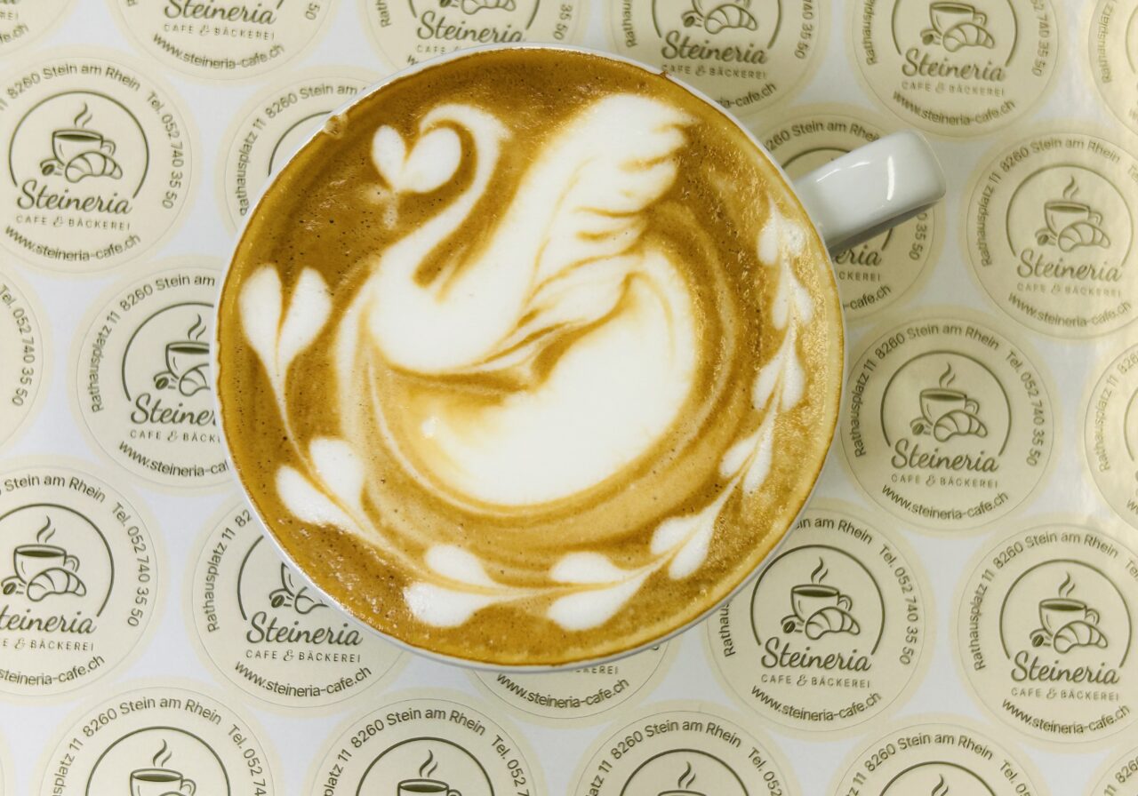 Cappuccino mit kunstvoller Schwan-Latte-Art auf Untersetzern von Steineria Café & Bäckerei, Stein am Rhein.