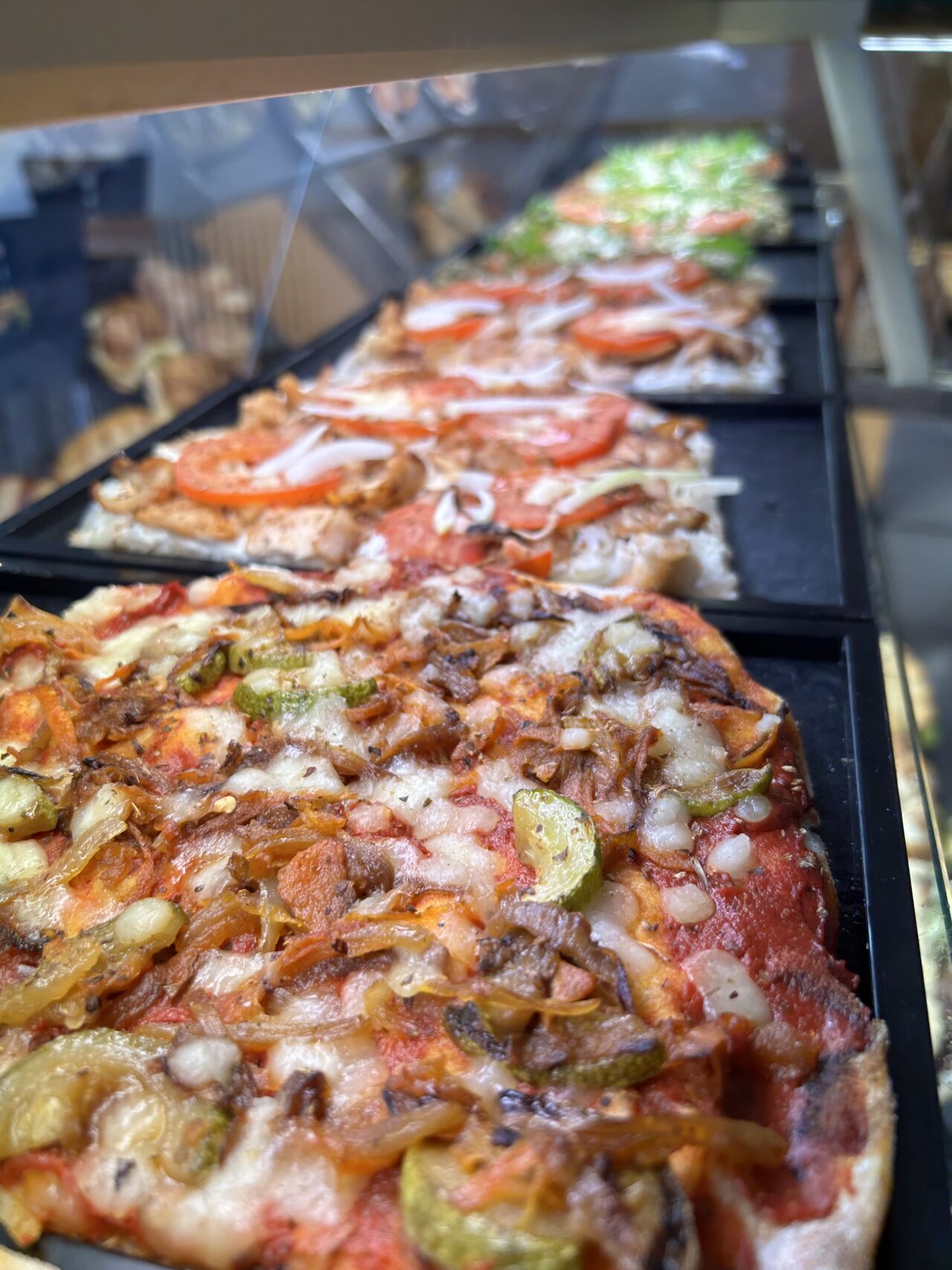 Nahaufnahme von frisch gebackenen Pizzen mit Gemüsebelag auf einem Blech, in einer Pizzeria präsentiert.