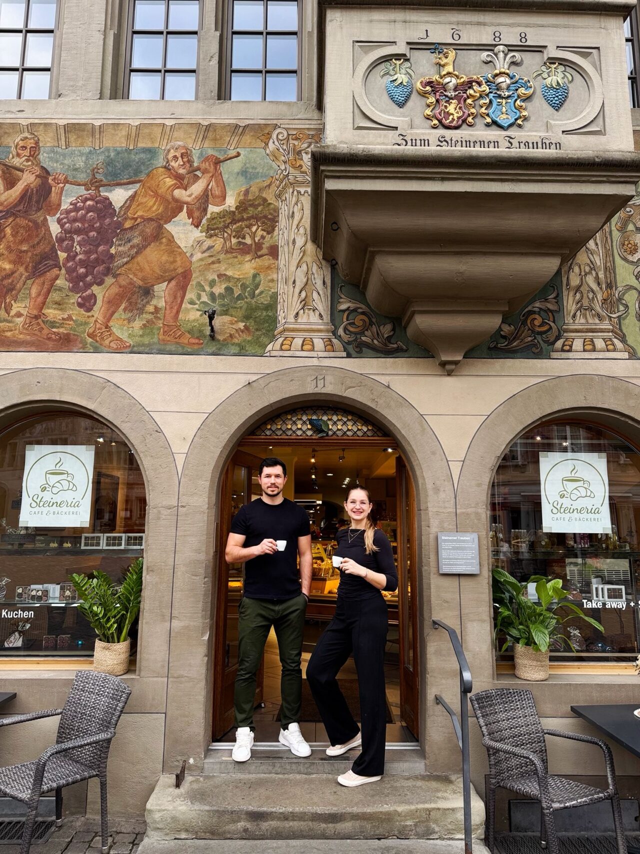 Menschen genießen Kaffee vor der Steineria Café & Bäckerei in historischer Umgebung.